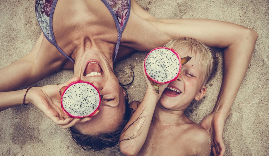 Mama und Sohn am Strand mit einer Drachenfrucht in der Hand Familien sparen