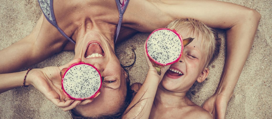 Mama und Sohn am Strand mit einer Drachenfrucht in der Hand Familien sparen